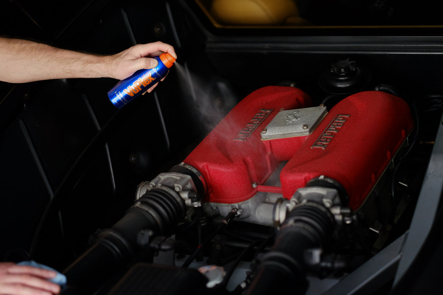 Man spraying VuPlex on a red engine in a car for cleaning and polishing.