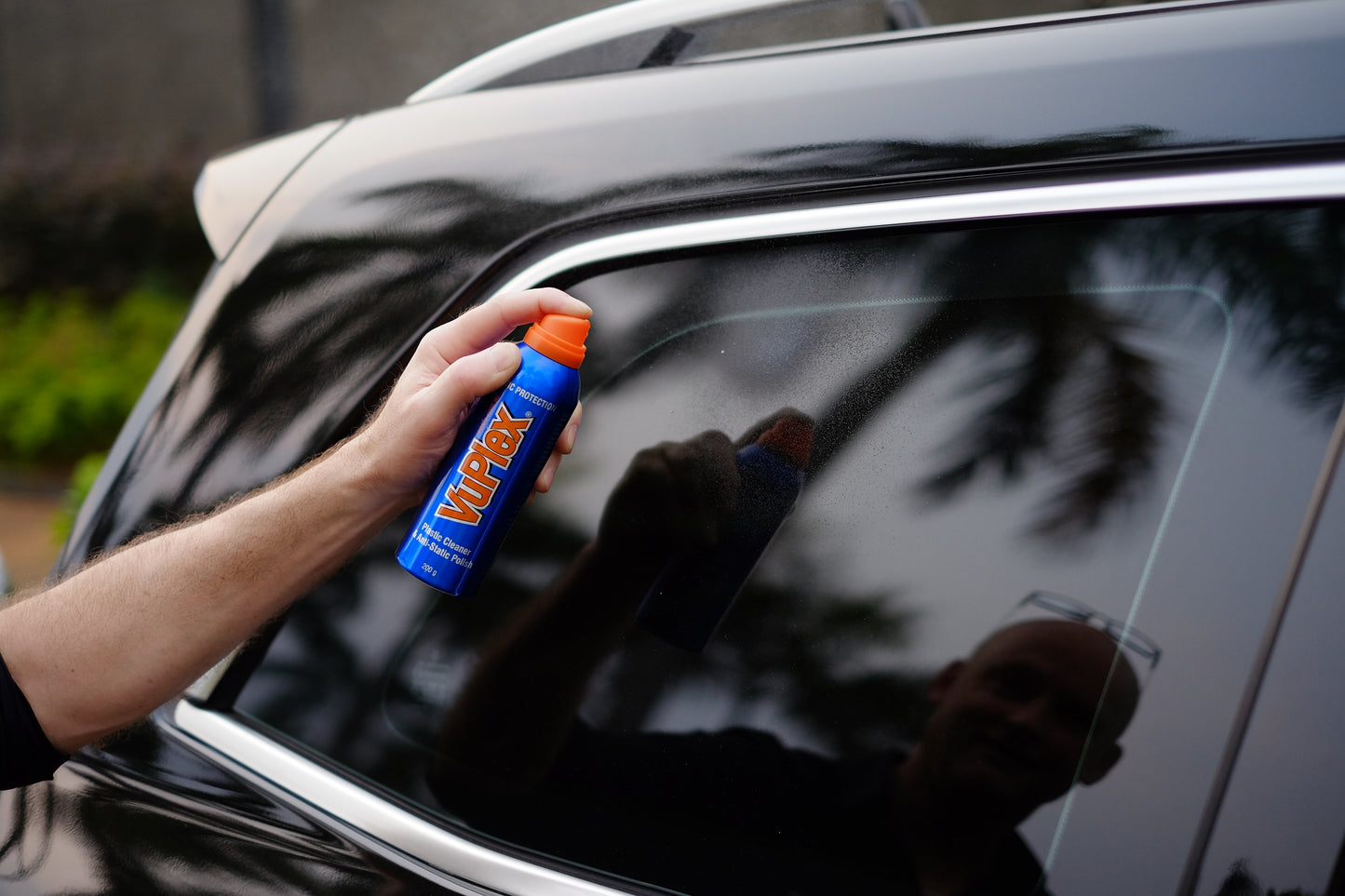 Hand holding VuPlex spray bottle for cleaning and polishing car windows.