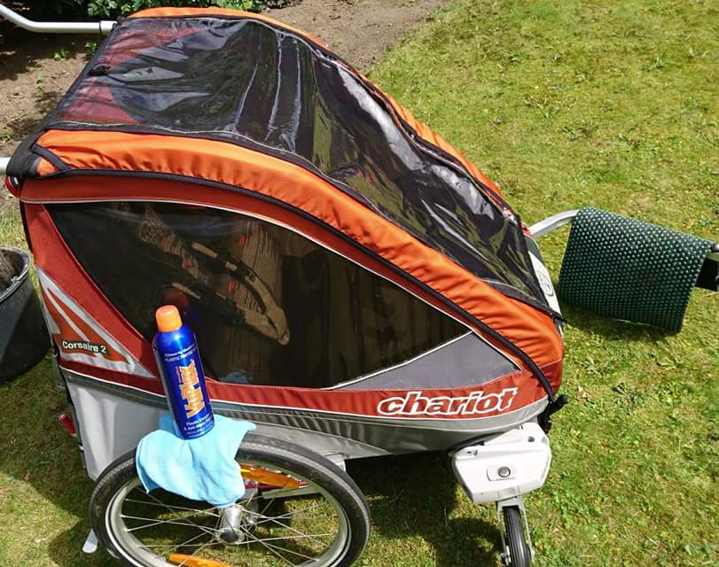 VuPlex Flasche neben einem Chariot Kinderanhänger im Garten zur Reinigung und Pflege von Kunststoffflächen.